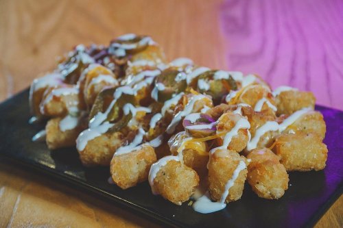 A plate of crispy tater tots topped with jalapeños, cheese, and drizzled with creamy sauce.