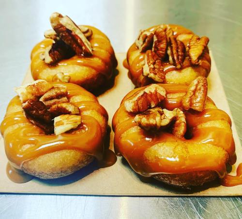 Four caramel-drizzled donuts topped with pecans on a brown paper tray.