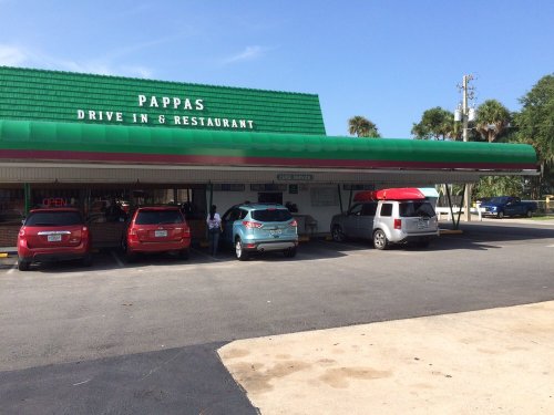 A drive-in restaurant with a green awning, featuring several parked cars and a clear blue sky.