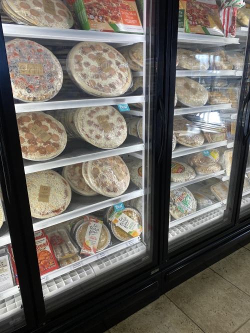 Frozen pizzas displayed in a glass-front refrigerator, showcasing various brands and flavors.