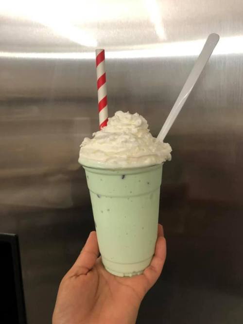 A hand holding a mint green milkshake topped with whipped cream and a red and white striped straw.