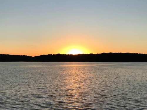 A serene sunset over a calm lake, with warm orange and yellow hues reflecting on the water's surface.