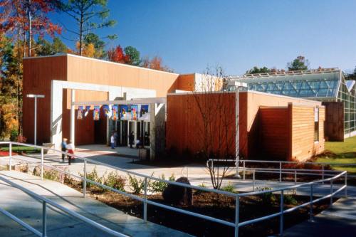 Modern building with wooden exterior, large glass windows, and colorful banners, surrounded by trees and landscaping.