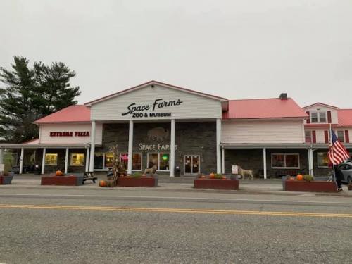 Front view of Space Farms Zoo & Museum, featuring a red roof, stone facade, and pumpkins outside.