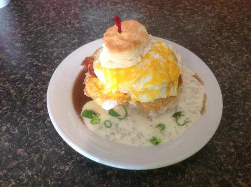 A hearty breakfast plate featuring a biscuit topped with cheese, fried egg, bacon, and creamy gravy, garnished with green onions.