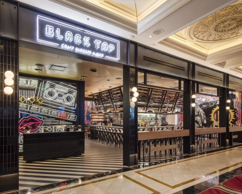 Exterior of Black Tap restaurant featuring neon signage, vibrant murals, and a modern design with a striped floor.