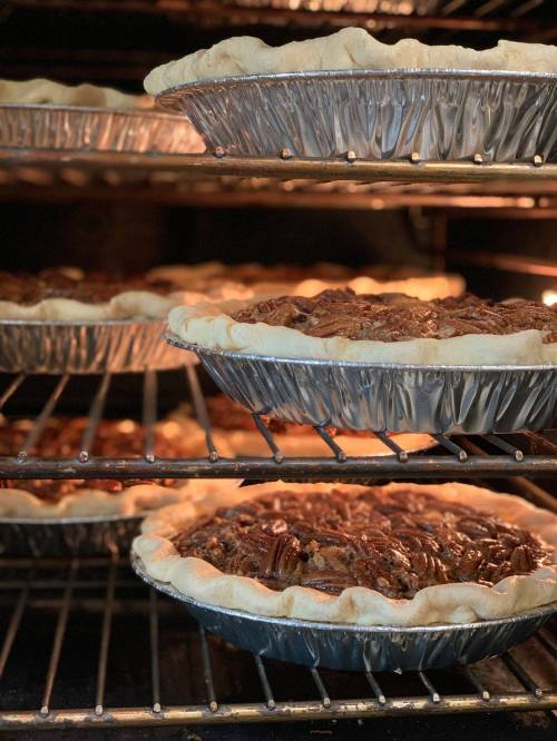 Three pies in metal pans baking in an oven, with golden crusts and rich fillings visible.