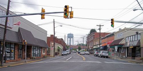 A small town street with shops, traffic lights, and a water tower in the background under a cloudy sky.