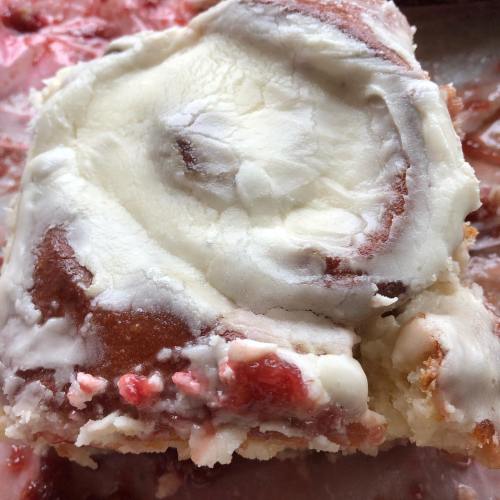 A close-up of a cinnamon roll topped with creamy frosting and a hint of strawberry filling.