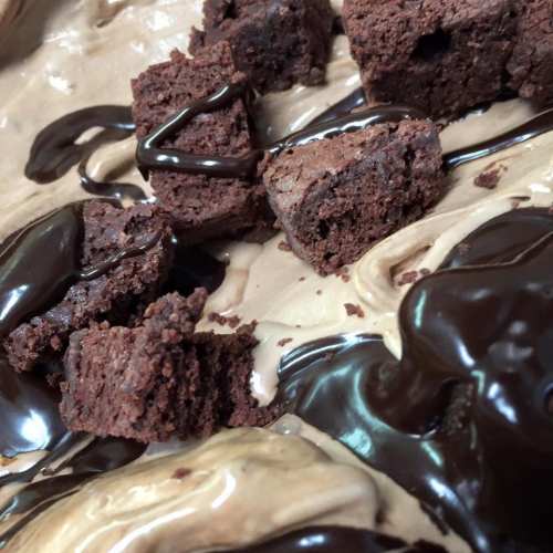 Close-up of chocolate brownies drizzled with dark chocolate sauce on a creamy dessert base.