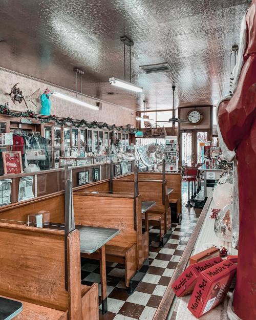 A vintage diner interior with wooden booths, checkered floor, and nostalgic decor, featuring a clock and old-fashioned displays.