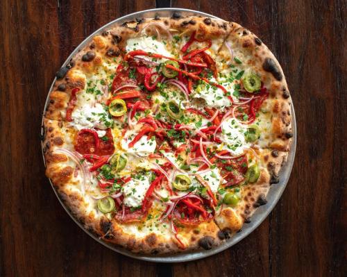 A freshly baked pizza topped with pepperoni, red peppers, onions, jalapeños, and dollops of ricotta on a golden crust.