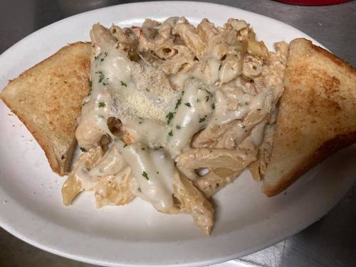 A plate of creamy pasta with penne, topped with cheese and herbs, served with two slices of toasted bread.