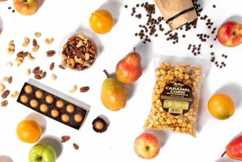 A variety of snacks including caramel corn, nuts, fruits, and chocolate arranged on a white background.