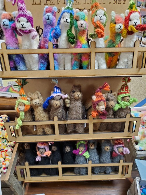 A display of colorful felted llama figurines wearing hats, arranged on a wooden stand.
