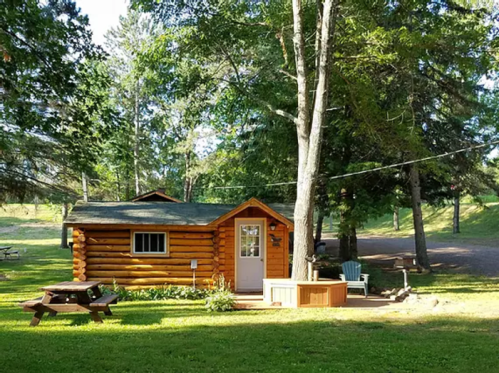 A cozy log cabin surrounded by trees, with a picnic table and chairs in a serene outdoor setting.