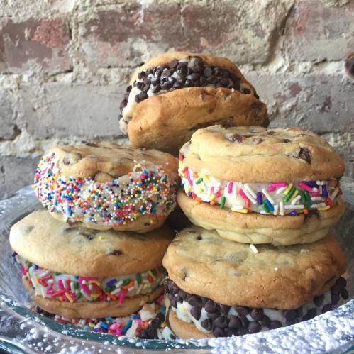 A plate of colorful cookie sandwiches filled with frosting and topped with sprinkles and chocolate chips.