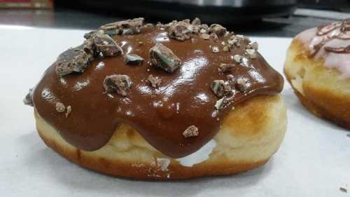A chocolate-glazed donut topped with crushed candy pieces, resting on a white surface.