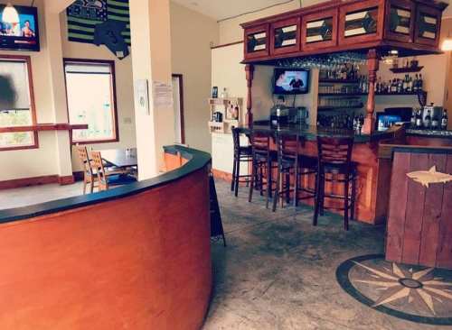 Interior of a bar with a wooden counter, high chairs, and a TV, featuring a nautical-themed design.
