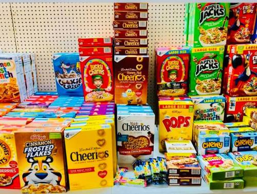 A colorful display of various cereal boxes, including Cheerios, Lucky Charms, and Frosted Flakes, on a store shelf.