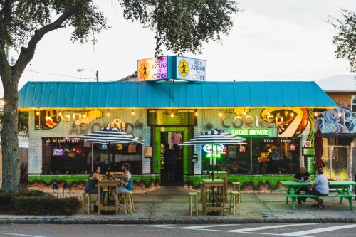 A vibrant brewery with outdoor seating, colorful signage, and patrons enjoying drinks on a sunny day.