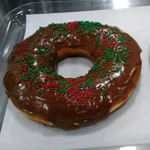 A large chocolate frosted donut topped with red and green sprinkles, resting on a white paper.