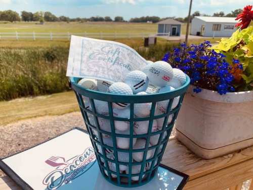 A teal basket filled with golf balls and a gift certificate, with a scenic outdoor background.