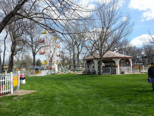A park scene featuring a Ferris wheel, gazebo, and green grass under a partly cloudy sky.