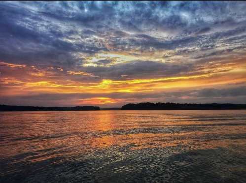 A serene sunset over a calm lake, with vibrant orange and purple hues reflecting on the water's surface.