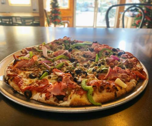 A freshly baked pizza topped with various meats, olives, and colorful vegetables on a silver serving tray.