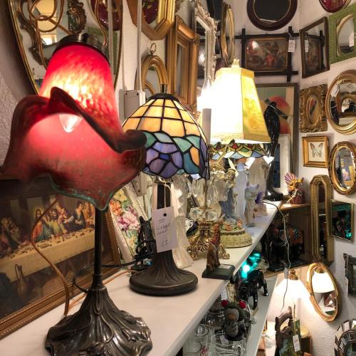 A collection of vintage lamps and framed mirrors displayed on a shelf in an antique shop.