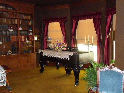 A vintage room featuring a grand piano, bookshelves, floral arrangement, and elegant curtains.