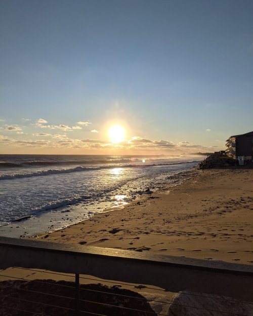A serene beach scene at sunset, with gentle waves and a golden sun reflecting on the water.