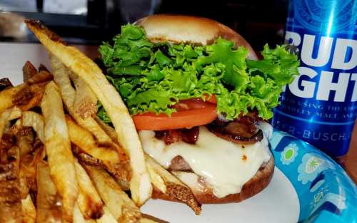 A juicy burger with lettuce, tomato, and bacon, served with crispy fries and a can of Bud Light.