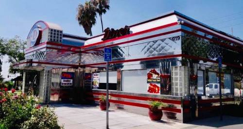 A shiny, retro-style diner with red and silver accents, surrounded by palm trees and blooming flowers.
