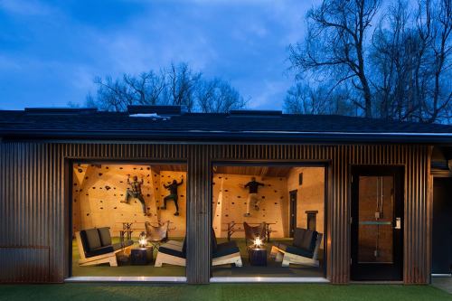 A modern climbing gym with two climbers on the wall, cozy seating, and a warm ambiance at dusk.