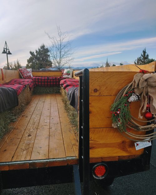 A wooden trailer with hay seating, decorated with plaid blankets and a festive wreath, set against a clear sky.