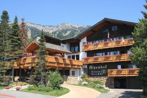 A charming mountain lodge with wooden balconies, surrounded by trees and mountains under a clear blue sky.