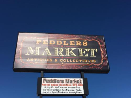 Sign for Peddlers Market, featuring antiques and collectibles, against a clear blue sky.