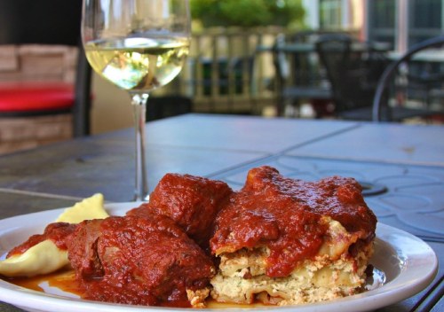 A plate of meatloaf topped with marinara sauce, served with mashed potatoes and a glass of white wine in the background.