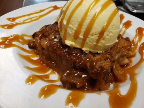 A slice of warm dessert topped with vanilla ice cream and drizzled with caramel sauce on a white plate.