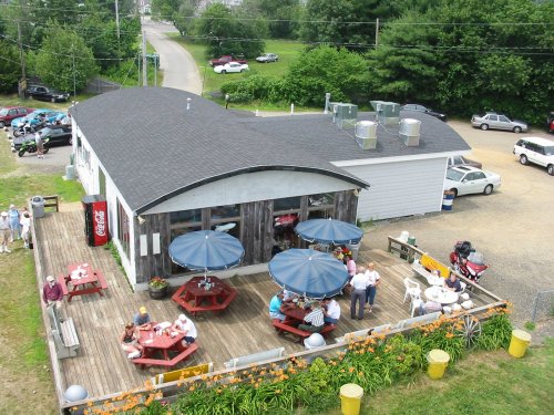 Aerial view of a restaurant with outdoor seating, umbrellas, and a parking area surrounded by greenery.