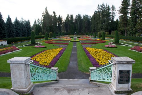 A beautifully landscaped garden with colorful flower beds, neatly arranged paths, and tall trees in the background.