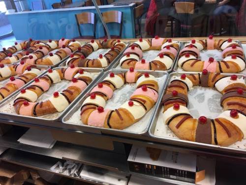 A display of colorful, decorated pastries arranged in trays, featuring pink, white, and chocolate icing with cherries on top.