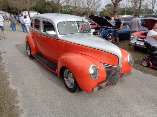 A classic orange and silver vintage car parked at a car show, surrounded by spectators and other vehicles.