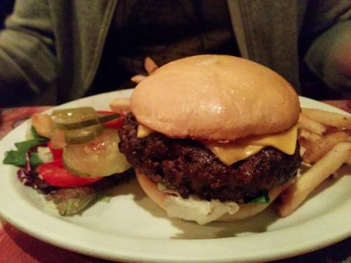 A cheeseburger with lettuce and pickles, served with a side of fries and a fresh salad on a white plate.