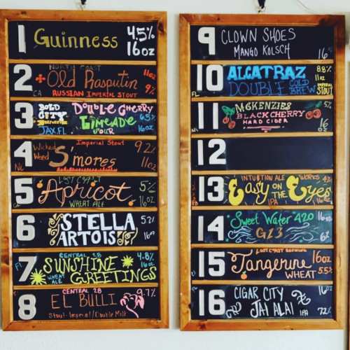 A chalkboard menu displaying various beers with names, styles, and alcohol percentages listed on two wooden boards.