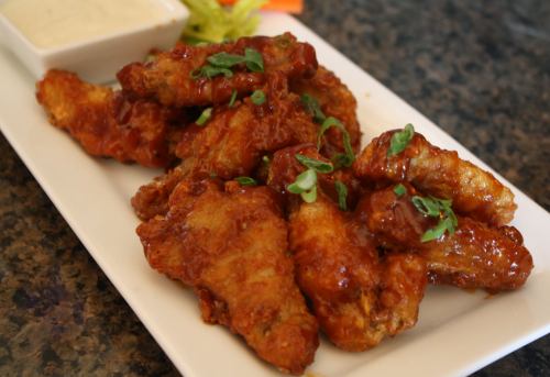 A plate of crispy, golden-brown chicken wings garnished with green onions, served with a side of dipping sauce.