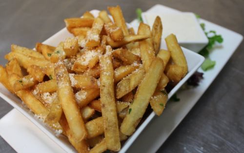 A bowl of golden, crispy French fries topped with grated cheese, served with a side of salad and dipping sauce.