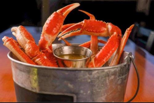A metal bucket filled with vibrant red crab legs and a small cup of dipping sauce.
